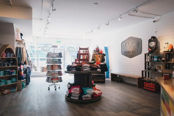 Interior of Dildo Brewing Co. Bottle Shop on Water Street, St. John's, with branded merchandise on hangers and shelves, and a large Dildo Brewing Co. logo on the wall.